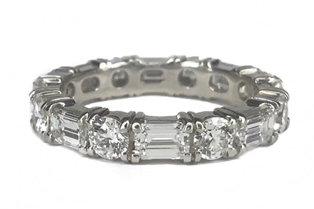 An eternity band features a combination of round-cut diamonds and emerald-cut diamonds