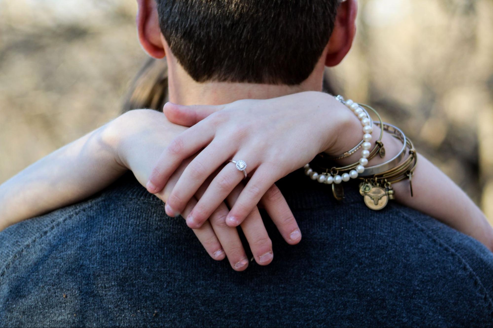 A woman wraps her arms around her partner&rsquo;s neck, wearing a variety of bracelets.