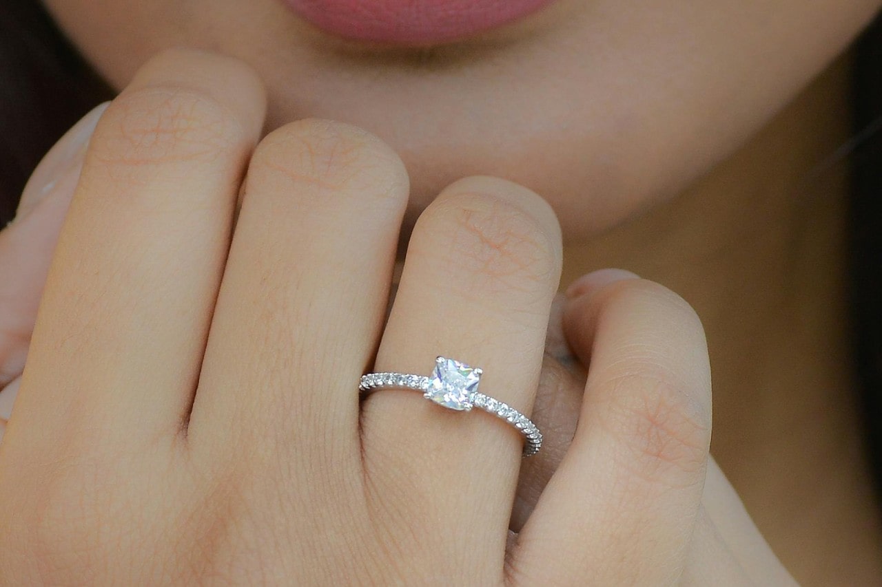 a woman&rsquo;s hand raised to her chin and adorned with a side stone engagement ring.