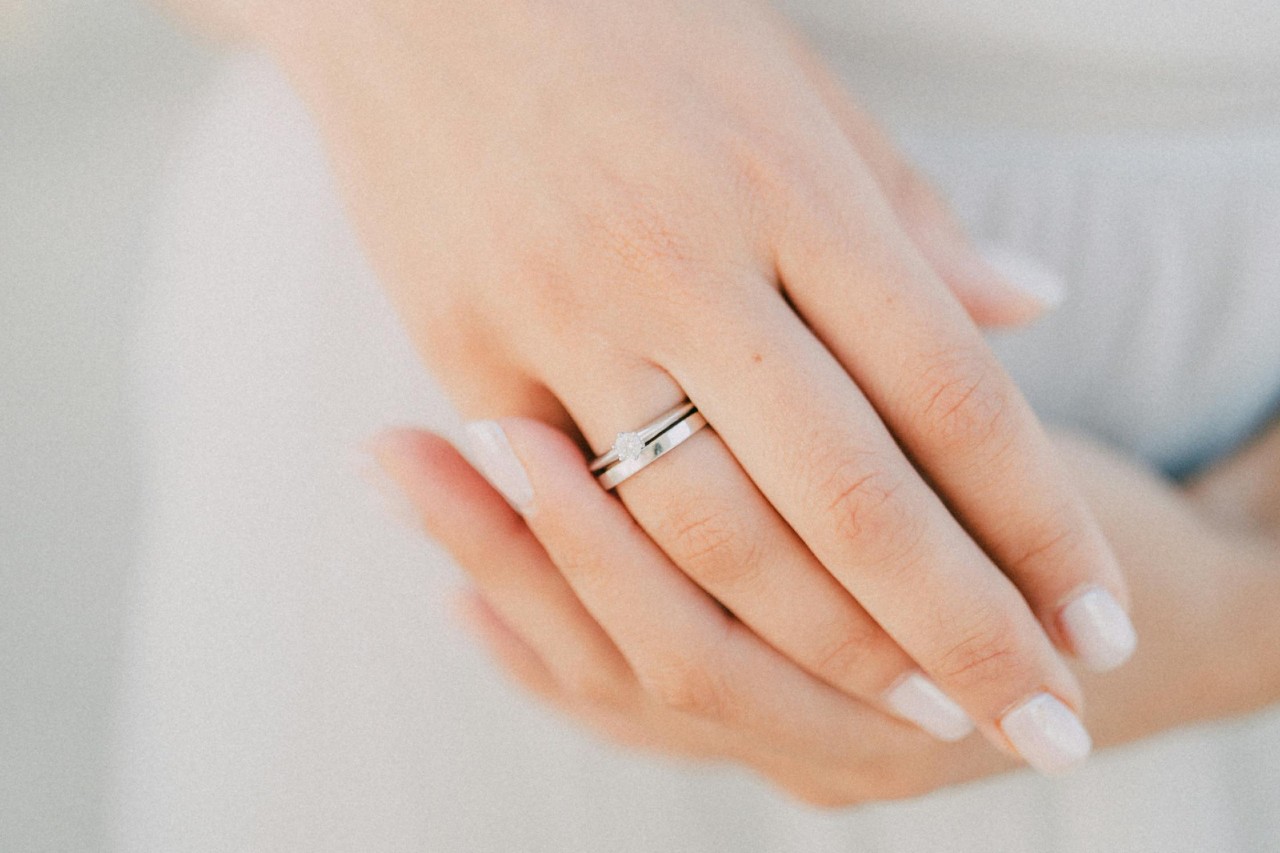 a woman’s hands adorned with a silver engagement ring and wedding band.