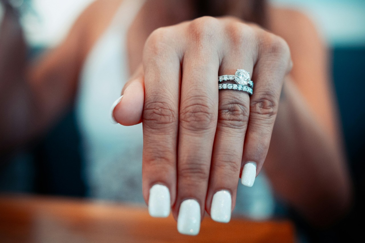 a woman&rsquo;s outstretched hand showing off a silver engagement ring and diamond wedding band.