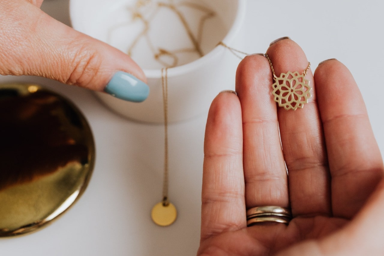 a woman&rsquo;s hand holding a yellow gold pendant necklace with a floral motif