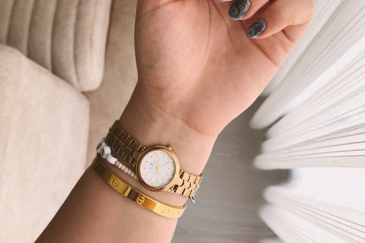 a woman&rsquo;s wrist wearing a yellow gold watch and two bracelets